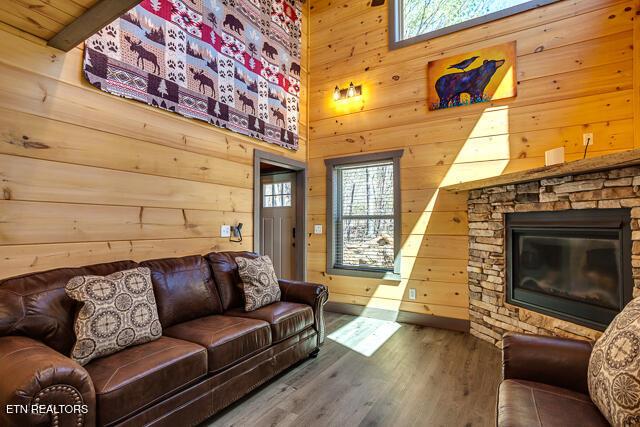 living area with a fireplace, wood finished floors, a wealth of natural light, and wooden walls