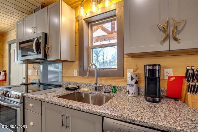 kitchen featuring wooden ceiling, light stone counters, stainless steel appliances, and a sink