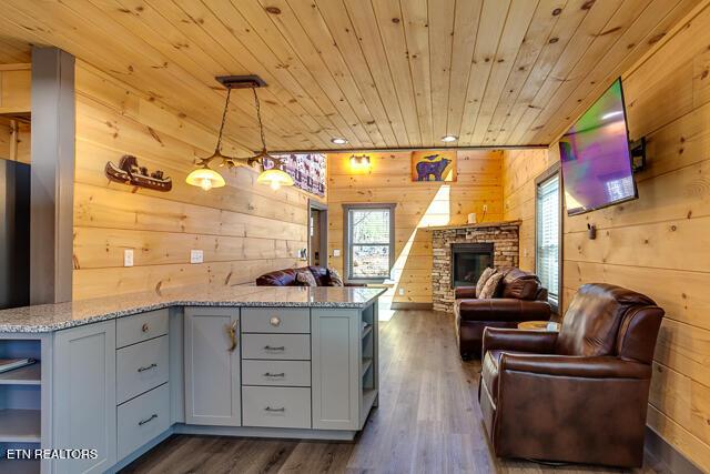 kitchen with wooden walls, dark wood finished floors, wood ceiling, a stone fireplace, and open shelves