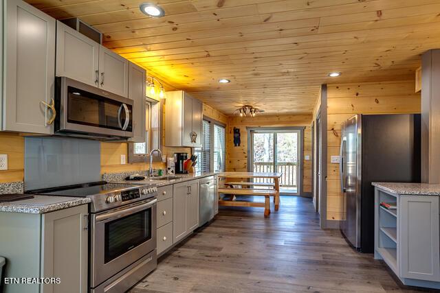 kitchen featuring wood ceiling, appliances with stainless steel finishes, wood finished floors, wood walls, and recessed lighting