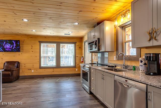 kitchen featuring light stone counters, wooden ceiling, dark wood-style flooring, a sink, and appliances with stainless steel finishes