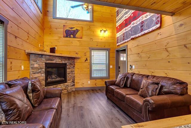 living room featuring a fireplace, wooden walls, a towering ceiling, and wood finished floors