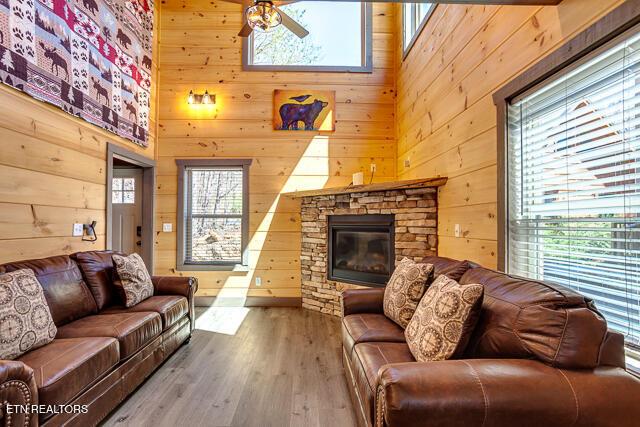 living room featuring a towering ceiling, ceiling fan, a stone fireplace, wooden walls, and wood finished floors