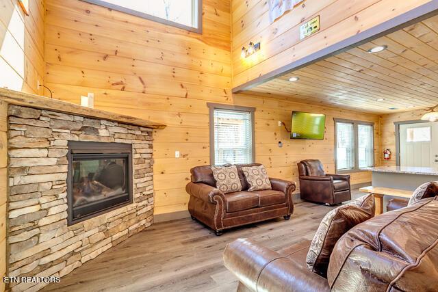 living area with light wood finished floors, plenty of natural light, wooden walls, and a stone fireplace