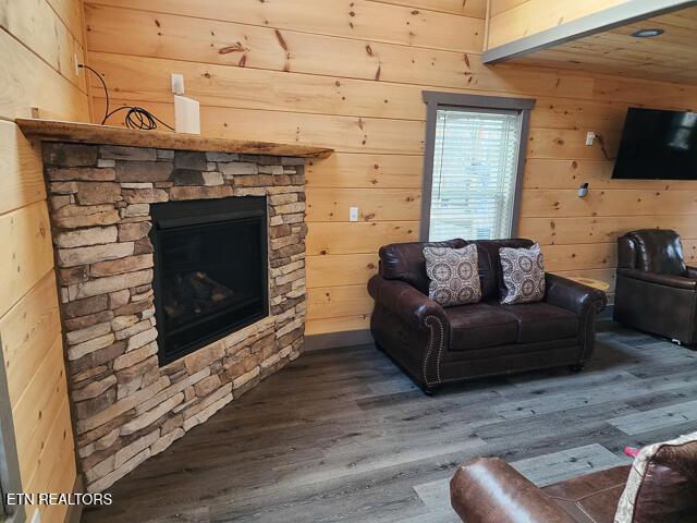 living room featuring a stone fireplace, dark wood-style flooring, and wooden walls