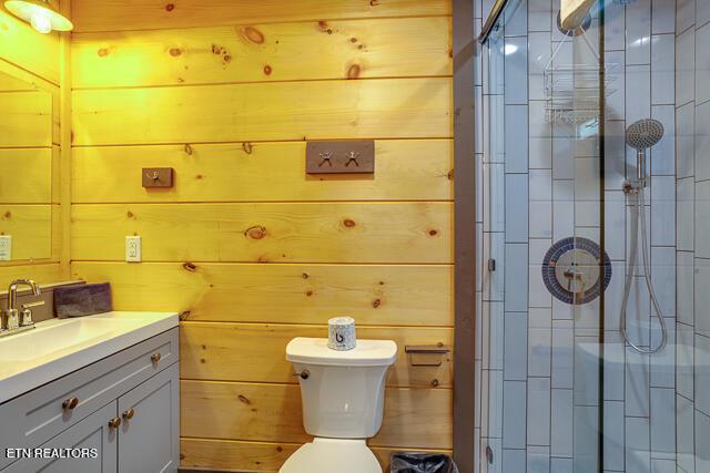 bathroom featuring wooden walls, a stall shower, vanity, and toilet