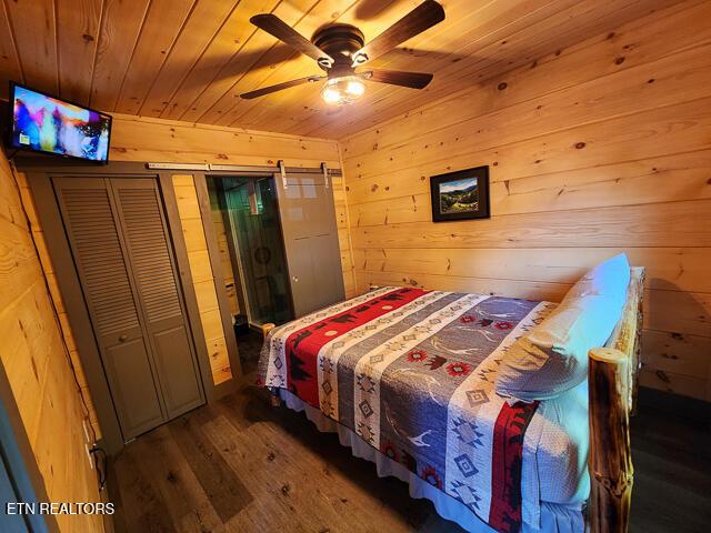 bedroom with a barn door, wooden ceiling, wood finished floors, and wooden walls