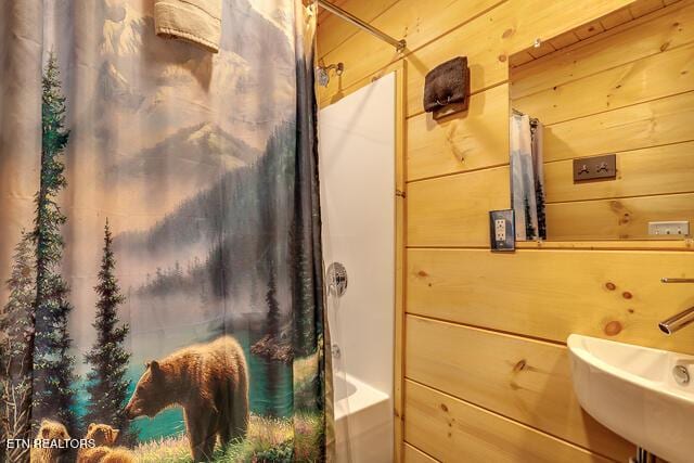 bathroom with shower / bath combination with curtain, a sink, and wooden walls