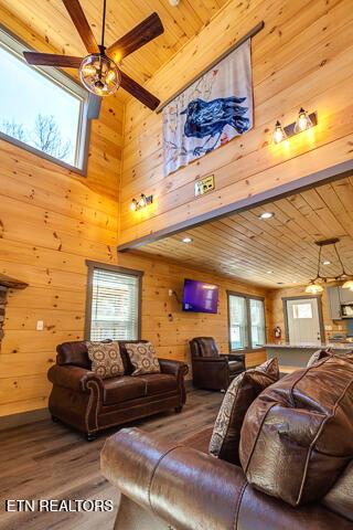 living area with a ceiling fan, wood ceiling, wood walls, and wood finished floors