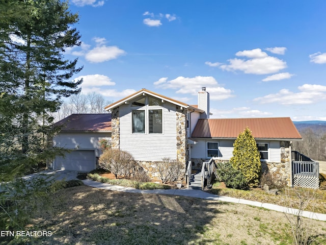 view of front facade featuring a garage, stone siding, a chimney, and metal roof