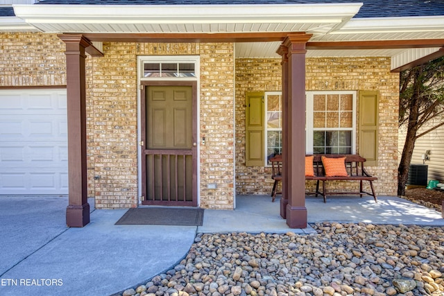 doorway to property featuring a garage, a porch, a shingled roof, and brick siding