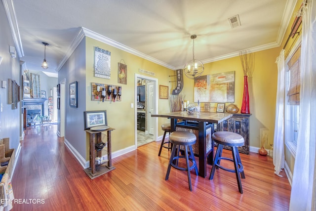 dining room featuring crown molding, visible vents, a stone fireplace, wood finished floors, and baseboards