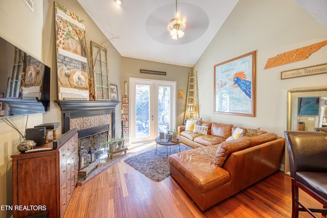 living area featuring high vaulted ceiling, a tiled fireplace, wood finished floors, and a ceiling fan