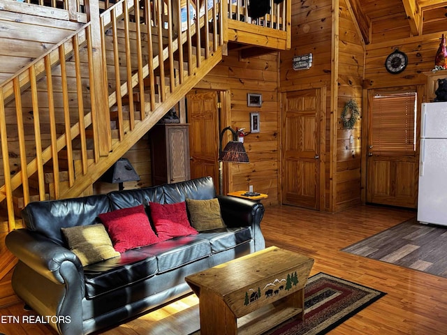 living area with stairway, high vaulted ceiling, wooden walls, and wood finished floors