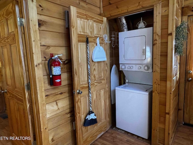 laundry area featuring stacked washer and dryer, laundry area, wood walls, and wood finished floors