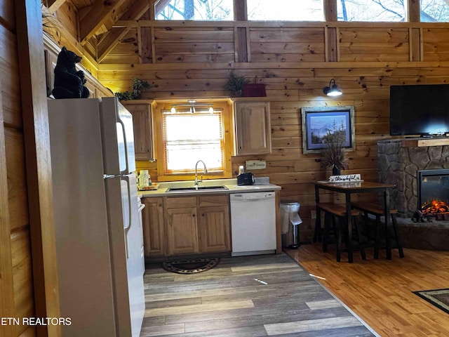 kitchen with white appliances, light wood-style flooring, a sink, and a stone fireplace