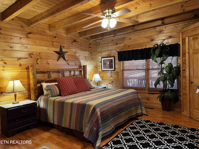 bedroom featuring wooden walls, beam ceiling, and wood finished floors