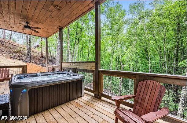 wooden terrace with ceiling fan, a hot tub, and a wooded view