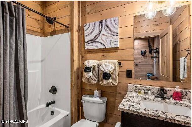 full bathroom featuring shower / bath combo with shower curtain, wooden walls, toilet, and vanity