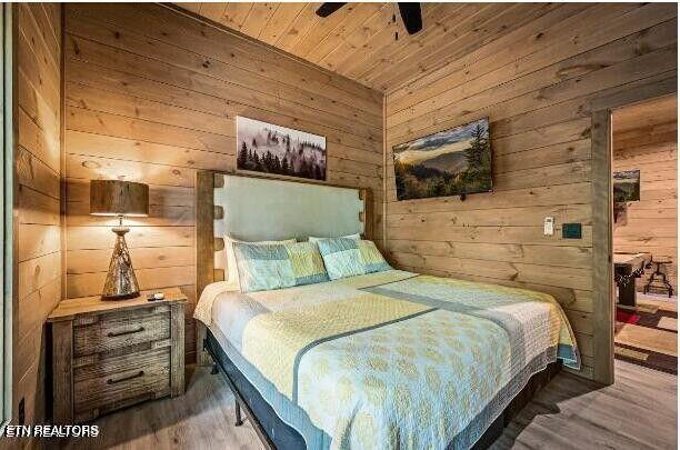 bedroom featuring a ceiling fan, wood ceiling, wooden walls, and wood finished floors