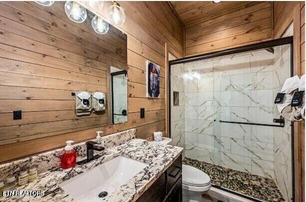 bathroom featuring toilet, a stall shower, wooden walls, and vanity