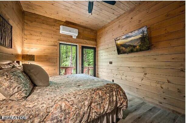 bedroom featuring wooden ceiling, a wall unit AC, ceiling fan, and wooden walls