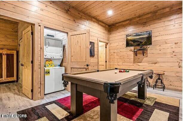 game room with wooden walls, light wood-type flooring, wooden ceiling, and stacked washer / drying machine