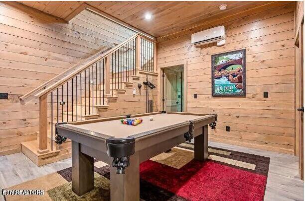 playroom with a wall mounted AC, wooden ceiling, light wood-style flooring, and wooden walls