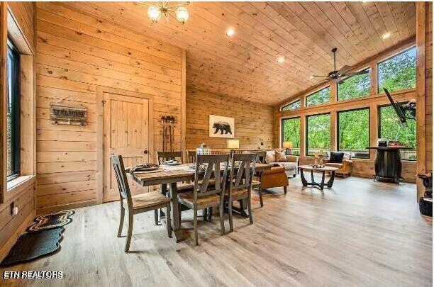 dining area with high vaulted ceiling, wood ceiling, light wood-style floors, and wooden walls