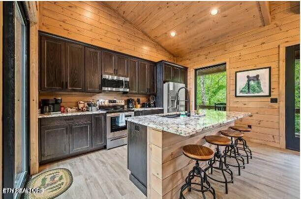 kitchen with lofted ceiling, wooden walls, stainless steel appliances, a sink, and wood ceiling