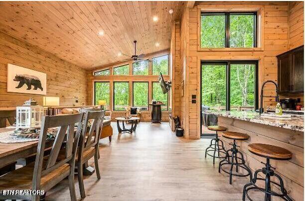 dining space featuring high vaulted ceiling, wooden ceiling, wood walls, and light wood-style flooring