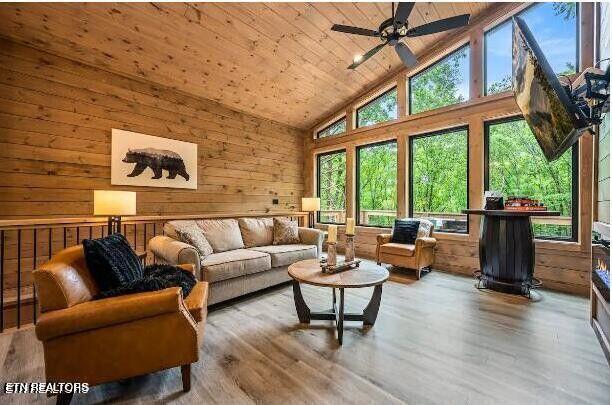 living area featuring a ceiling fan, wooden walls, wood finished floors, high vaulted ceiling, and wooden ceiling