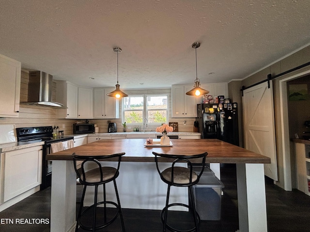 kitchen with wall chimney exhaust hood, butcher block counters, a barn door, a sink, and black appliances