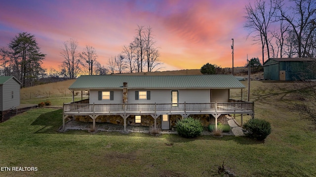 back of house at dusk featuring a yard, metal roof, a deck, stone siding, and an outdoor structure