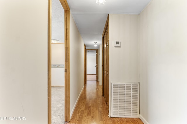 corridor featuring light wood finished floors, baseboards, and visible vents