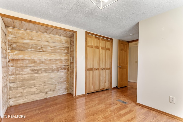 unfurnished bedroom with a textured ceiling, light wood-style flooring, visible vents, and baseboards