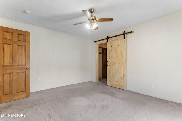 carpeted empty room featuring ceiling fan and a barn door