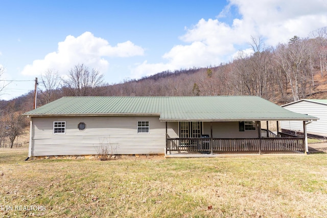 back of property with metal roof, covered porch, a lawn, and a view of trees