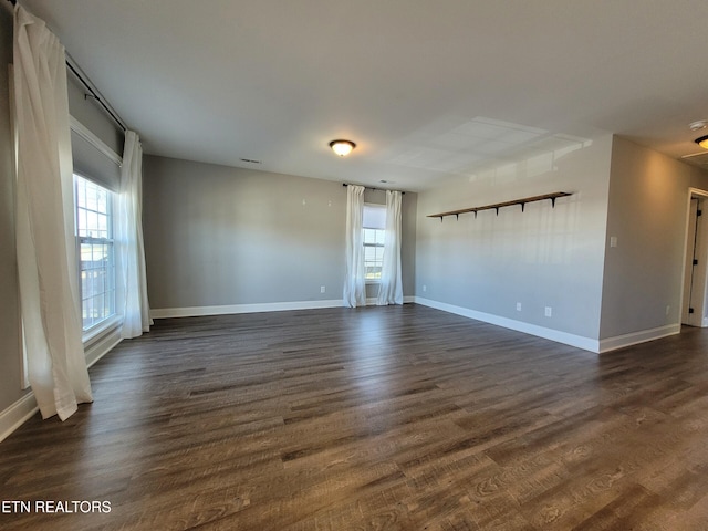 empty room featuring dark wood-style floors, visible vents, and baseboards