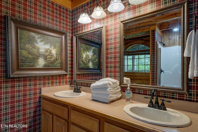 bathroom with double vanity, wallpapered walls, and a sink