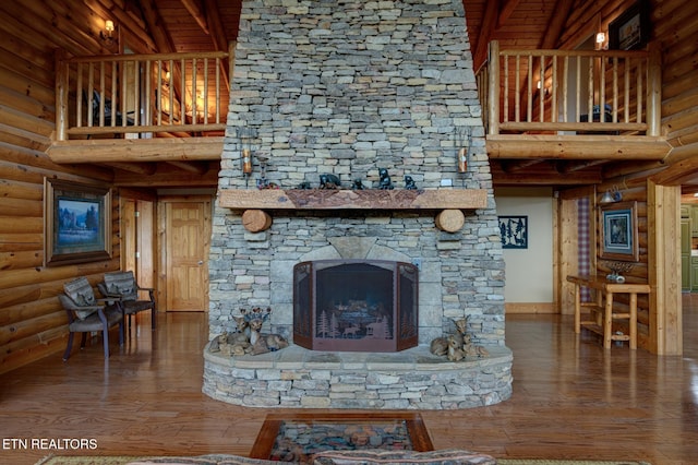 unfurnished living room with log walls, a stone fireplace, a high ceiling, and wood finished floors