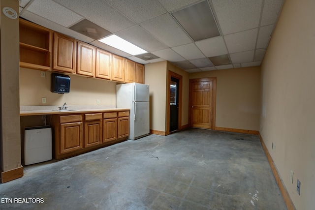 kitchen featuring freestanding refrigerator, light countertops, a drop ceiling, and baseboards