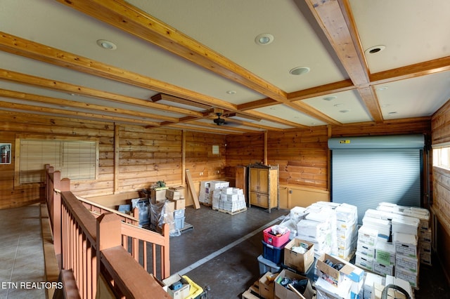 misc room with wood walls, a ceiling fan, beam ceiling, and an upstairs landing