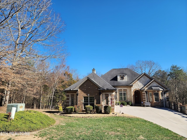 french country style house featuring stone siding, driveway, roof with shingles, and a front yard