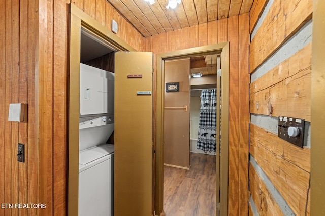 clothes washing area with stacked washer and dryer, laundry area, wood ceiling, wood finished floors, and wood walls