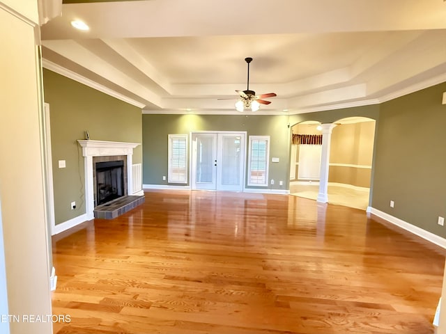 unfurnished living room featuring ornate columns, baseboards, a tray ceiling, and arched walkways