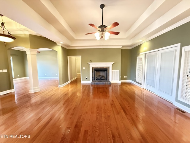 unfurnished living room featuring arched walkways, a raised ceiling, decorative columns, and wood finished floors