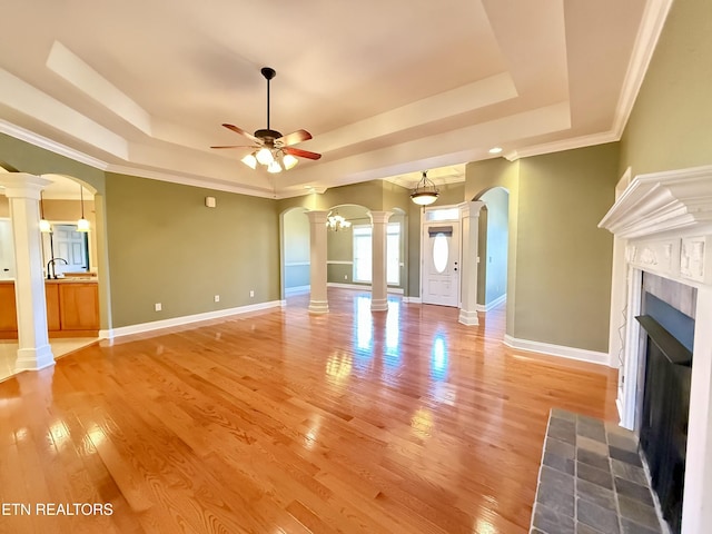 unfurnished living room with arched walkways, a tiled fireplace, a raised ceiling, and decorative columns