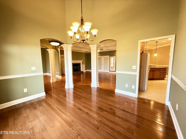 unfurnished dining area featuring light wood finished floors, decorative columns, a high ceiling, and arched walkways