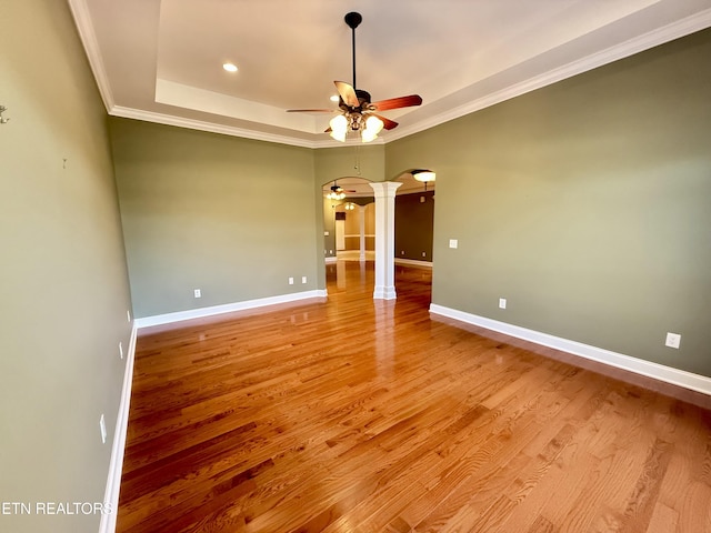 unfurnished room with arched walkways, a tray ceiling, crown molding, and baseboards